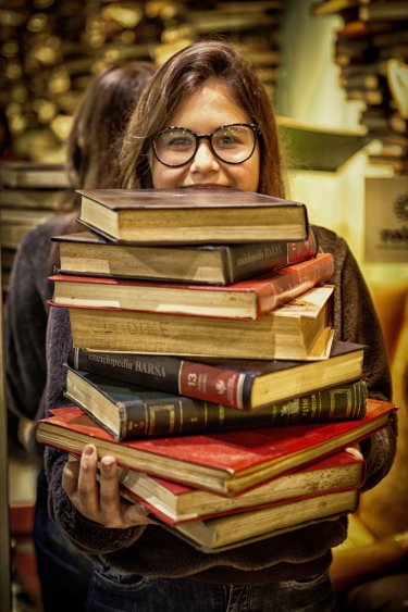 Imagem de menina carregando uma porção de livros classicos antigos de cor preta e vermelha, nas mãos